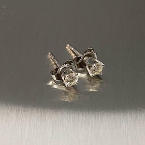 May include: A pair of stud earrings featuring round, clear, faceted stones set in a four-prong silver-toned metal setting. Each earring includes a thin post and a butterfly-style back, showcasing a classic design with reflective surfaces.