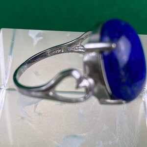 Op de afbeelding: Een zilveren ring met een grote, ovale, donkerblauwe edelsteen. De ring heeft een delicaat, opengewerkt ontwerp.