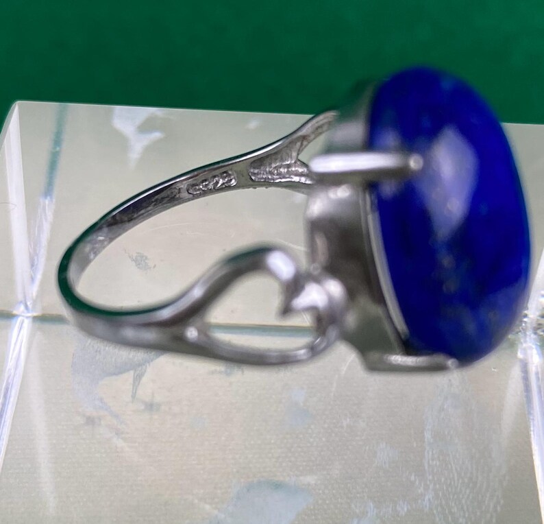 Op de afbeelding: Een zilveren ring met een grote, ovale, donkerblauwe edelsteen. De ring heeft een delicaat, opengewerkt ontwerp.