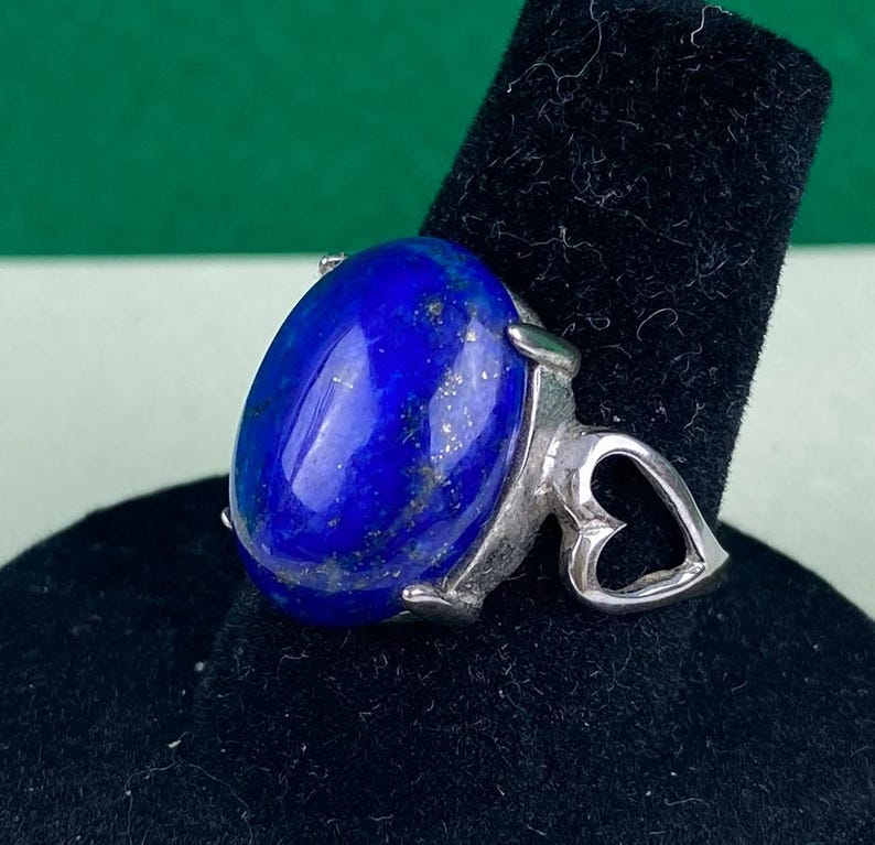 Op de afbeelding: Een zilveren ring met een grote ovale lapis lazuli-edelsteen. De ring heeft een hartvormig ontwerp op de band.