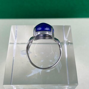 Op de afbeelding: Een zilveren ring met een grote, ovale blauwe edelsteen gezet in een zilveren zetting.