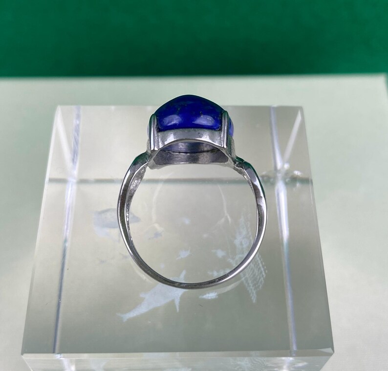 Op de afbeelding: Een zilveren ring met een grote, ovale blauwe edelsteen gezet in een zilveren zetting.