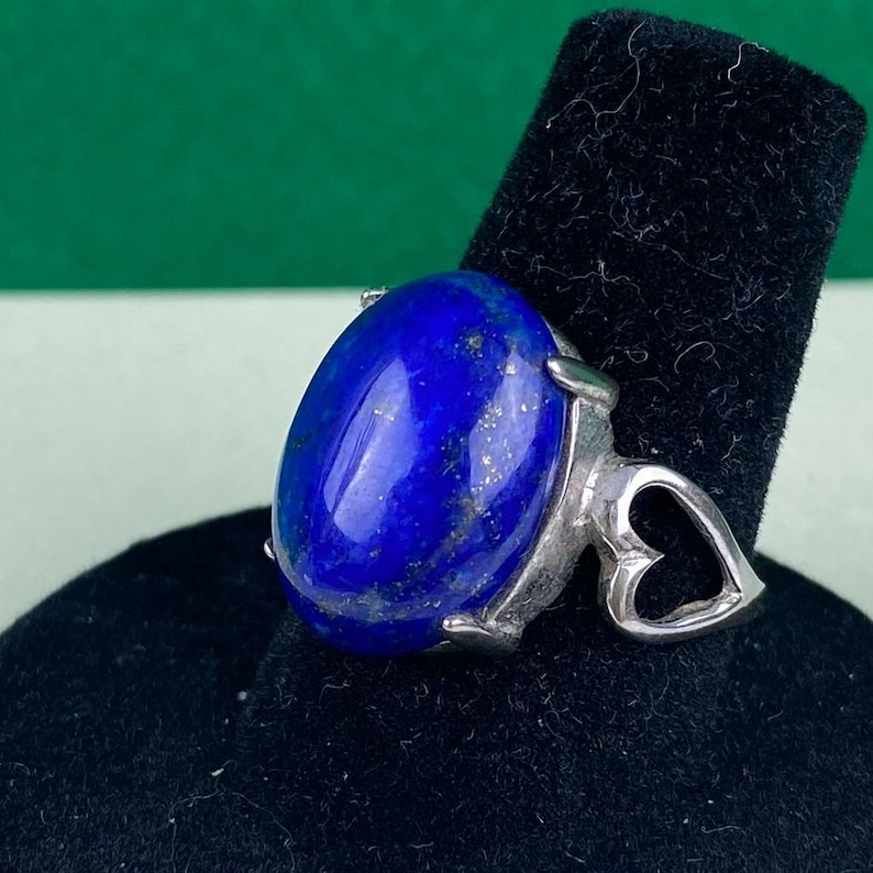 Op de afbeelding: Een zilveren ring met een grote ovale lapis lazuli-edelsteen en een hartvormig ontwerp op de band.