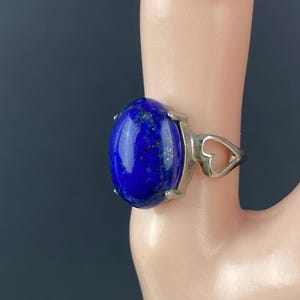 Op de afbeelding: Een zilveren ring met een grote ovale lapis lazuli-steen. De ring heeft een hartvormig ontwerp op de band.