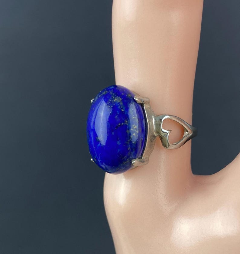 Op de afbeelding: Een zilveren ring met een grote ovale lapis lazuli-steen. De ring heeft een hartvormig ontwerp op de band.