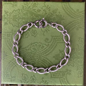 May include: A silver chain bracelet with a textured oval link design. The bracelet has a lobster claw clasp.