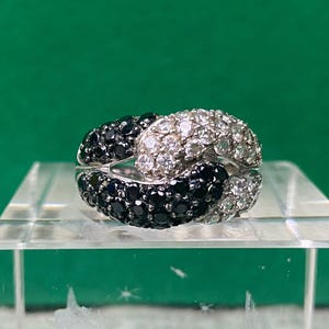 May include: A silver ring with black and white stones set in a knot design.