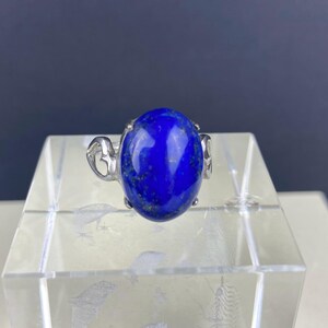 Op de afbeelding: Een zilveren ring met een grote, ovale lapis lazuli-edelsteen. De ring heeft een delicaat, versierd ontwerp.