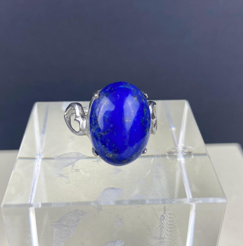 Op de afbeelding: Een zilveren ring met een grote, ovale lapis lazuli-edelsteen. De ring heeft een delicaat, versierd ontwerp.
