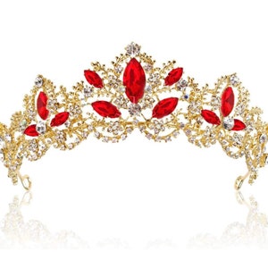 Puede incluir: Una tiara dorada con diamantes de imitación rojos y transparentes. La tiara tiene un diseño floral delicado.