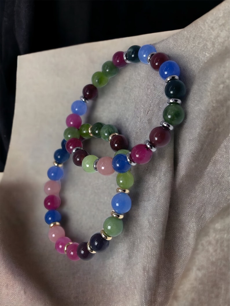 May include: Two colorful beaded bracelets with alternating shades of pink, green, blue, and purple. The beads are separated by silver and gold spacers.