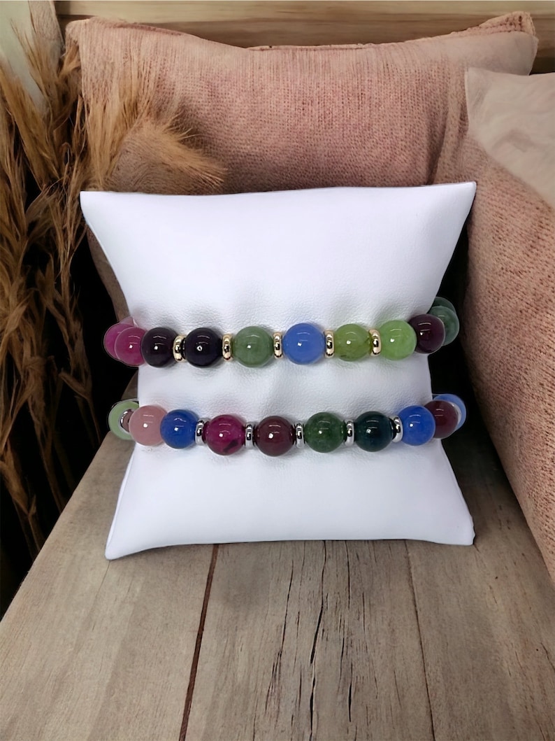 May include: Two bracelets with colorful gemstone beads. The top bracelet has green, blue, and purple beads with gold accents. The bottom bracelet has pink, green, blue, and purple beads with silver accents.