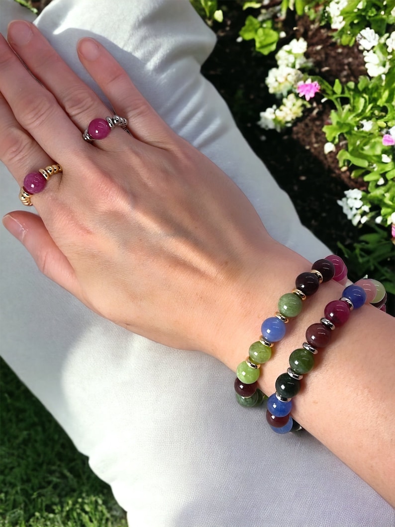 May include: Two bracelets with colorful round beads. One bracelet has green, blue, and purple beads. The other bracelet has green, red, and blue beads.