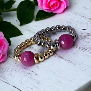 May include: Two beaded rings with pink gemstone accents. The rings are made of gold and silver beads.