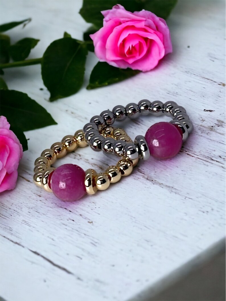 May include: Two beaded rings with pink gemstone accents. The rings are made of gold and silver beads.