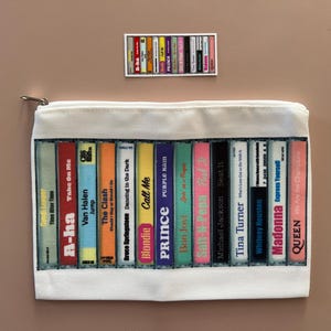 May include: White zippered pouch with a colorful print of cassette tapes featuring the names of various artists, including A-ha, Van Halen, The Clash, Blondie, Prince, Bon Jovi, Michael Jackson, Tina Turner, Whitney Houston, Madonna, and Queen.