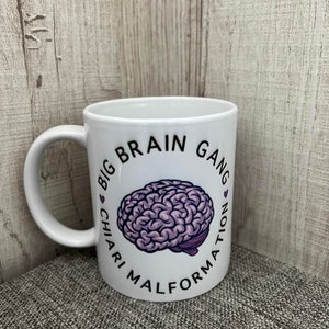 May include: White ceramic mug with a black and purple design. The design features a brain with the text "Big Brain Gang Chiari Malformation" around it.