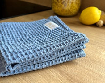 Op de afbeelding: Een stapel blauwe wafelstructuur keukendoeken gevouwen op een houten oppervlak.