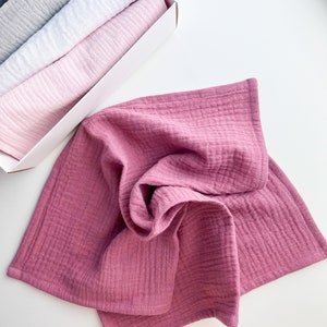 Peut inclure: Un ensemble de quatre linges en mousseline douce et textur&eacute;e dans des tons de rose, blanc, gris et bleu. Les linges sont pli&eacute;s et empil&eacute;s dans une bo&icirc;te blanche.