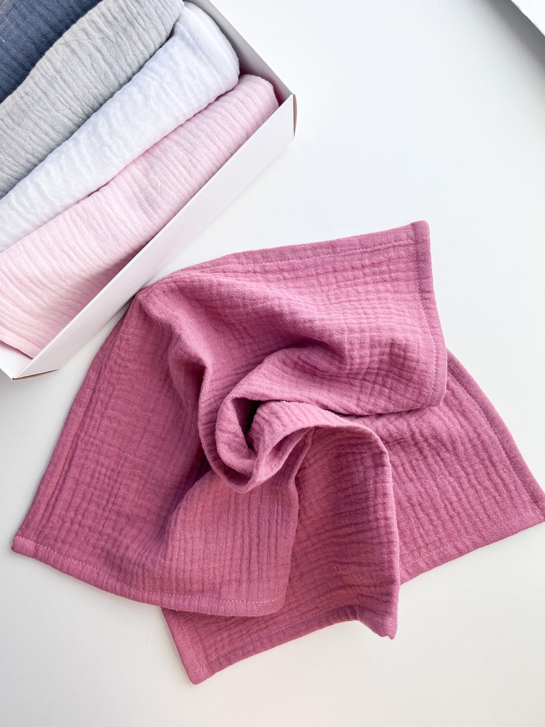 Peut inclure: Un ensemble de quatre linges en mousseline douce et textur&eacute;e dans des tons de rose, blanc, gris et bleu. Les linges sont pli&eacute;s et empil&eacute;s dans une bo&icirc;te blanche.