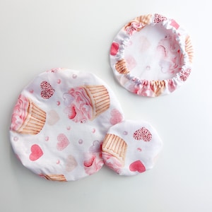 Può includere: Tre copri ciotola in tessuto rosa e bianco con un motivo a cupcake e cuore. I coperchi sono di dimensioni diverse.