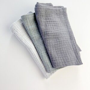 Peut inclure: Trois linges en mousseline de coton pli&eacute;s ensemble. Le linge du dessus est gris fonc&eacute;, le linge du milieu est gris clair et le linge du dessous est blanc.