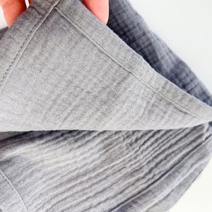 Peut inclure: Une couverture en mousseline grise avec un bord cousu. La couverture est pli&eacute;e en deux et le tissu est textur&eacute;.