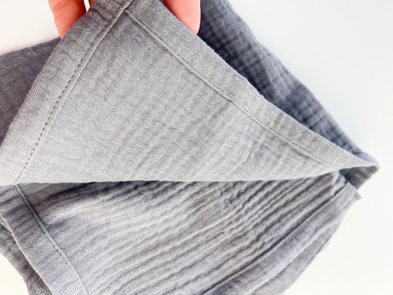 Peut inclure: Une couverture en mousseline grise avec un bord cousu. La couverture est pli&eacute;e en deux et le tissu est textur&eacute;.