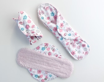 May include: Three reusable cloth menstrual pads with a floral print in pink, blue, and white. The pads are folded and ready to use.