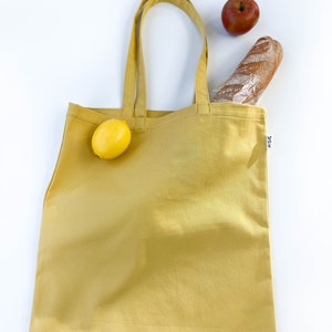 May include: A yellow tote bag with a lemon, a baguette, and an apple inside. The bag has a small tag with the word "F24" on it.
