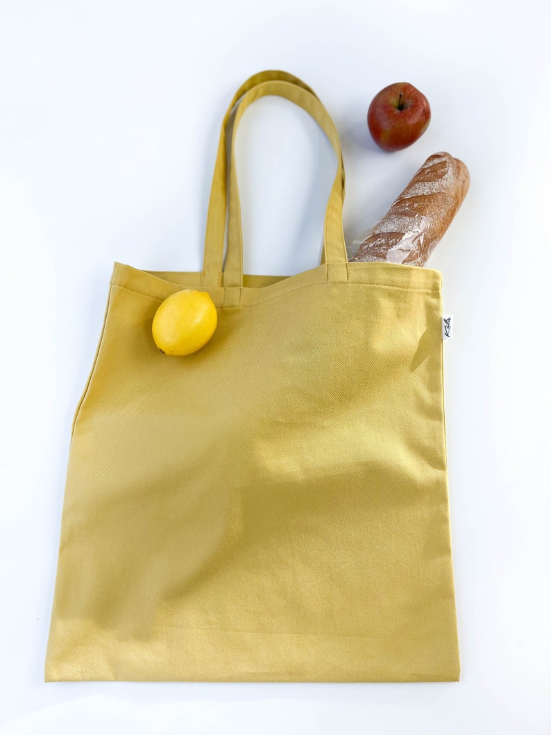 May include: A yellow tote bag with a lemon, a baguette, and an apple inside. The bag has a small tag with the word "F24" on it.