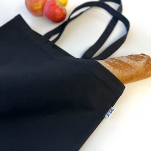May include: A black reusable tote bag with a single baguette inside. The bag has two black straps and a white label with the word "Kila" printed on it.