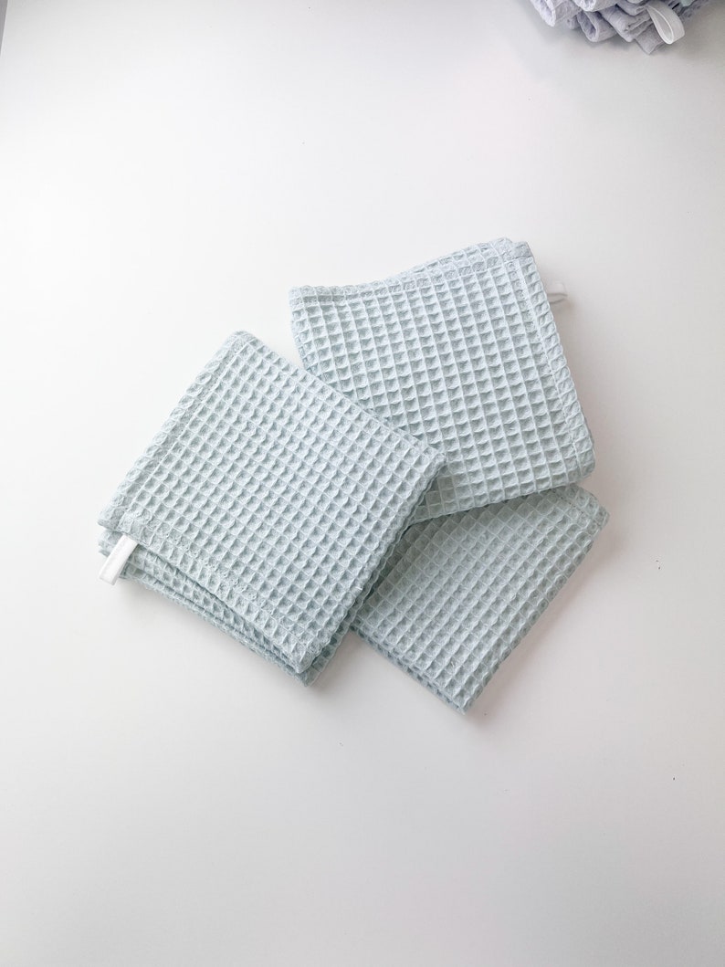 May include: Four light blue waffle weave kitchen towels stacked on a white surface.