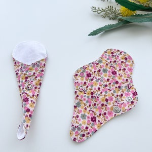 May include: Two reusable cloth menstrual pads with a floral print in shades of pink, yellow, and gray. The pads have snaps along the edges.