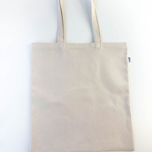 May include: A plain white canvas tote bag with a small black logo on the bottom right corner.