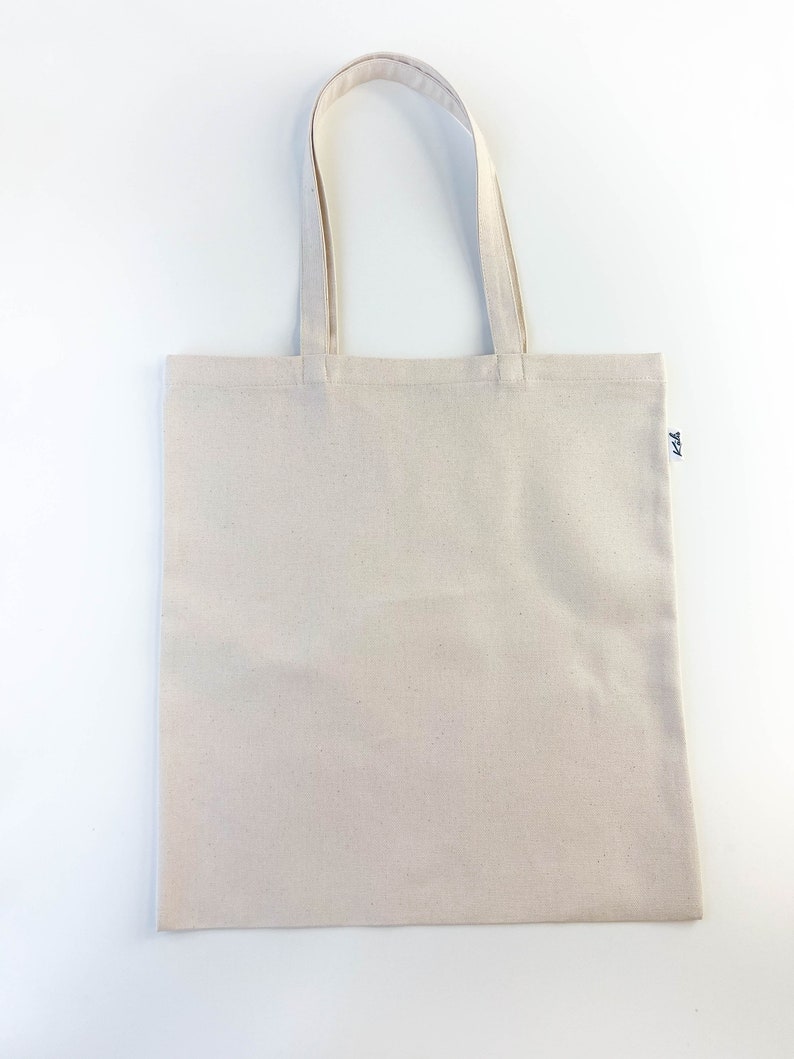 May include: A plain white canvas tote bag with a small black logo on the bottom right corner.