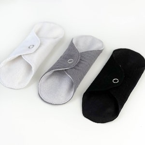 May include: Three reusable cloth menstrual pads in white, gray, and black. Each pad has a snap closure and is folded in half.
