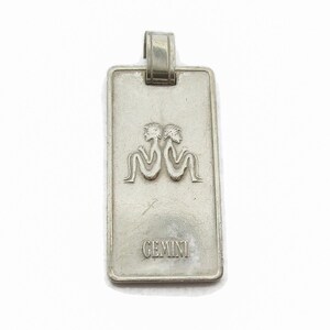 Puede incluir: Encanto de colgante de plata con un s&iacute;mbolo del zod&iacute;aco G&eacute;minis y la palabra "GEMINI" grabada en la parte delantera.