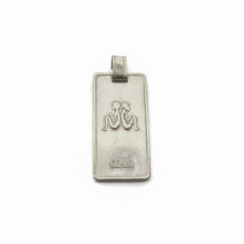 Puede incluir: Encanto de colgante de plata con un s&iacute;mbolo del zod&iacute;aco G&eacute;minis y la palabra "GEMINI" grabada en la parte delantera.