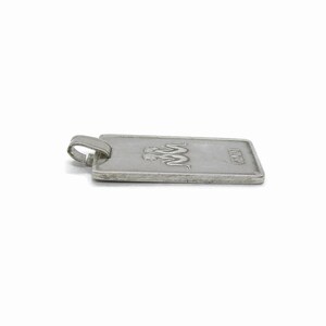 Puede incluir: Pendiente de plata con forma rectangular y un logotipo de dos serpientes entrelazadas con la palabra "JUNO" grabada en la parte inferior.