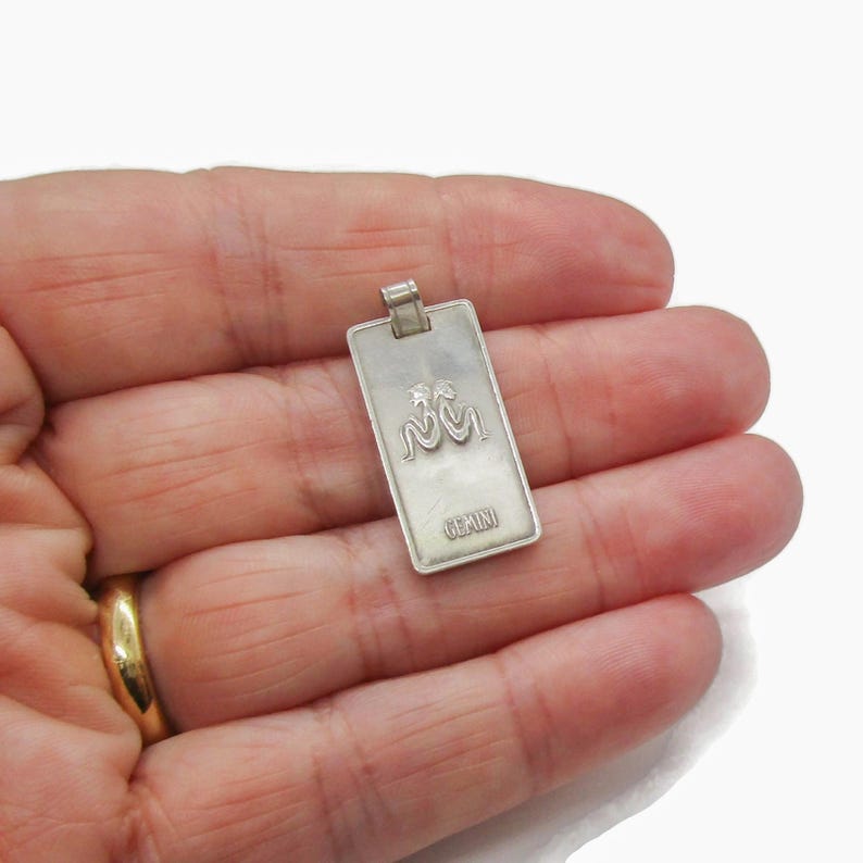 Puede incluir: Encanto de colgante de plata con el signo del zod&iacute;aco G&eacute;minis y la palabra "G&eacute;minis" inscrita debajo.