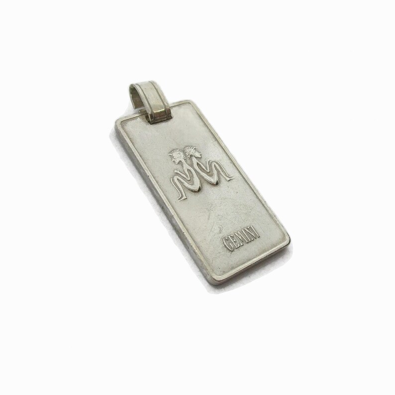 Puede incluir: Encanto de colgante de plata con el s&iacute;mbolo del zod&iacute;aco G&eacute;minis y la palabra "GEMINI" inscrita debajo.