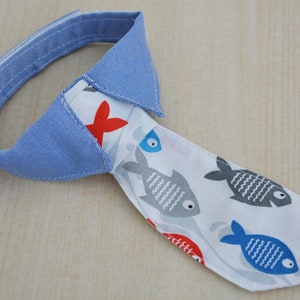May include: A blue and white fabric tie with a fish pattern. The tie has a blue collar with white stitching.