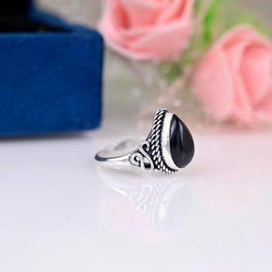 Puede incluir: Un anillo de plata con una piedra negra en forma de lágrima. El anillo tiene detalles intrincados alrededor de la piedra.