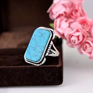 May include: A silver ring with a rectangular turquoise stone set in a decorative border.