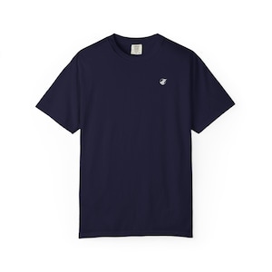 May include: A navy blue short-sleeve t-shirt with a crew neckline. The shirt features a small, circular white graphic logo on the upper left chest area. The interior neck label displays the text Comfort Colors with size information visible.