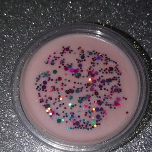 May include: A round wax melt in a clear container with a pink wax base and colourful glitter.