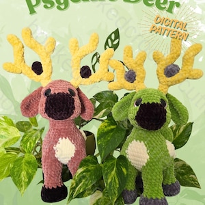 May include: Two crocheted deer toys, one pink and one green, with yellow antlers and black and white accents. The text "Psychic Deer" and "Digital Pattern" are displayed above the toys. The toys are surrounded by green foliage.