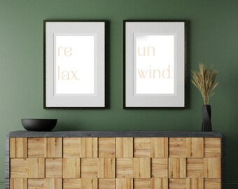 Puede incluir: Dos impresiones enmarcadas con las palabras "relax" y "unwind" en color beige claro sobre un fondo blanco. Las impresiones están colgadas en una pared verde oscuro sobre un armario de madera con tapa negra.