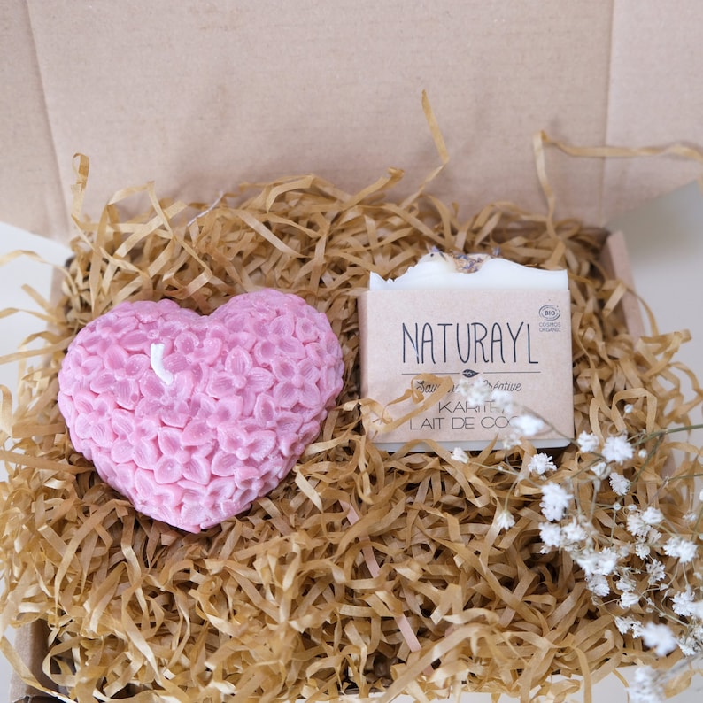 K&ouml;nnte beinhalten: Eine braune Geschenkbox aus Papier, gef&uuml;llt mit zerkn&uuml;lltem Papier, mit einer rosa herzf&ouml;rmigen Kerze und einer Seife. Die Seife ist wei&szlig; mit einer Lavendelbl&uuml;te obenauf und dem Text "NATURAYL" in Schwarz. Die Seife tr&auml;gt auch den Text "KAKAO LAIT DE CO" in Schwarz.